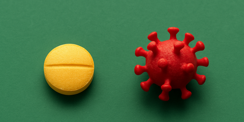 Gelbe Vitamin-D-Tablette und rotes Modell des Coronavirus auf grünem Hintergrund – Symbolbild für den Zusammenhang zwischen Vitamin D und COVID-19.